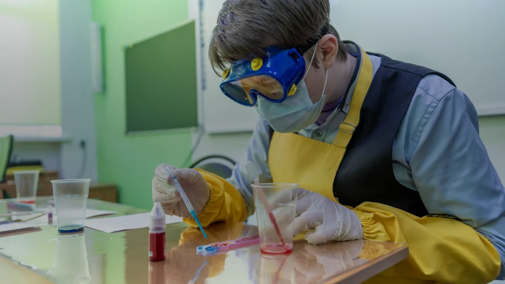 Élève en lunettes de protection réalisant une manipulation au laboratoire