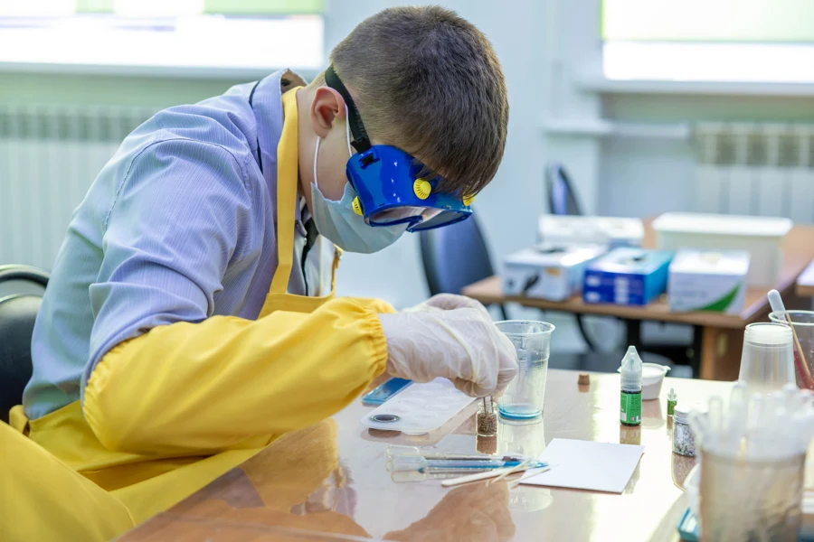 Élève en blouse et lunettes de protection qui réalise une manipulation de chimie à sa paillasse