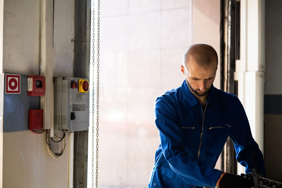 Technicien en tenue de travail bleue devant un coffret électrique avec arrêt d'urgence